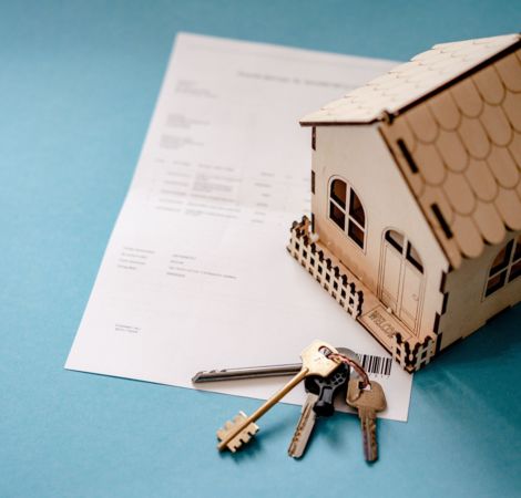 Ein Modellhaus steht auf einem Kaufvertrag. Daneben liegt ein Schlüssebund mit einem Hausschlüssel.